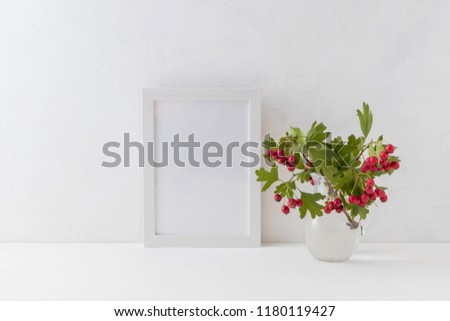 Mockup white frame and branches with red berries in a vase on a light background
