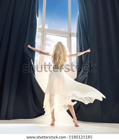 Young woman opens curtains at the window