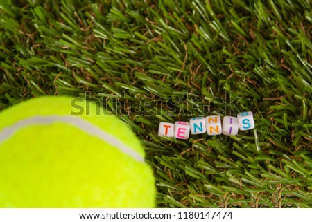 The word tennis is made up of cubes with colored letters lying on the green grass next to the tennis ball
