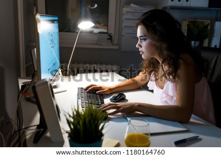Woman working late at night at home. Pretty young student sitting at desk and doing her homework, she is connecting to the internet. Woman look at computer screen at night