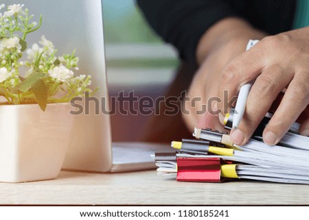 Businessman hands holding pen working in Stacks of paper files searching info unfinished documents achieves with  business report papers, Professional work for financial document on computer in office