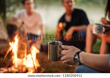 close up cropped photo. focus on the man's hand holding metal cup. hikers on the blurred background of the photo
