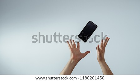 A view of the hand that tosses or catches a mobile phone. The smartphone is falling, hands are trying to catch it. The concept of communication, attempts to connect and talk. Royalty-Free Stock Photo #1180201450