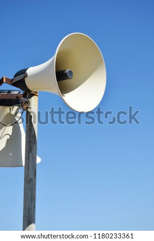 Old weathered vintage public address (PA) megaphone system loudspeaker and blue sky.