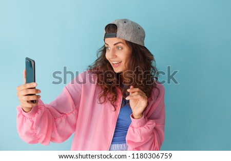 Portrait of a cheerful curly brunette with long hair with cap in her head and a pink jacket makes herself a photo