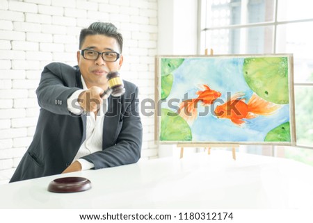 Handsome young Asian man in black suite, auctioneer, holding gavel, wooden hammer, bidding goldfish watercolor painting picture. Successful close deal of business trading of hobby fish pet art concept