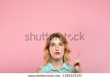 look up. free space for advertising above young woman. girl pointing up with her index finger. pink background for speech balloon.