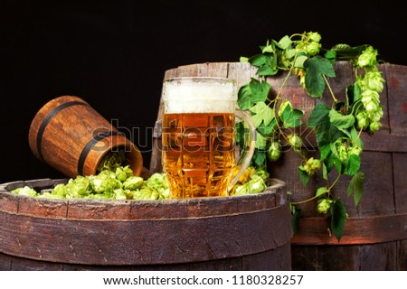 A mug of beer and hops on an old barrel .