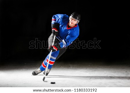 Young hockey player with stick and puck skating on rink in attack against dark background