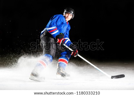 Hockey player with stick turning around skating on ice against black background