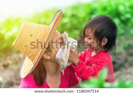 Happy asian family on garden fields with Background Concept. Little daughter be holding a hat closed her mom face on natural light.