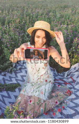 Beautiful young woman taking a selfie on the field of clover, soft focus background