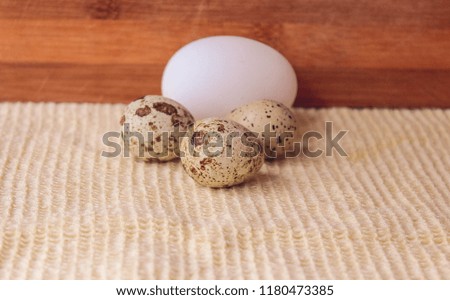 Three quail eggs and one chicken egg on wooden background