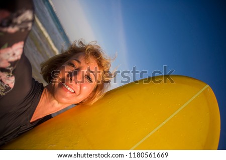 young attractive and happy blonde surfer woman in swimsuit holding surf board in the beach taking self portrait selfie picture smiling cheerful enjoying holidays at tropical island