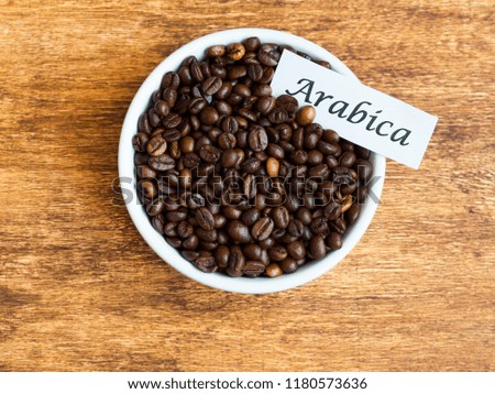 Bowl with Arabica coffee beans on wooden background, flat lay