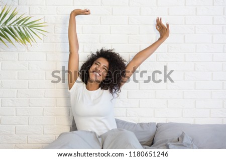 Beautiful african-american woman waking up in her bed, smiling and stretching, copy space Royalty-Free Stock Photo #1180651246