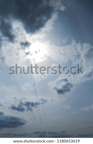 Cloudy sky with a bright sun, contrails, shadows, and a low light halo.