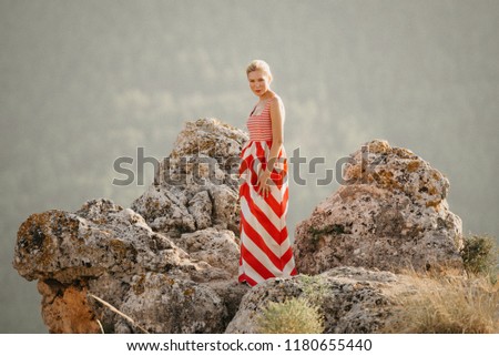 A cute blonde lady in the red and white dress dancing with on the top of the cliff with the mountain in the background. Mountain view. Evening in Spain