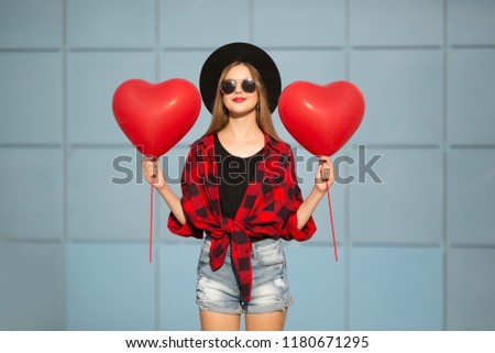 woman on blue wall background. Woman with balloons in black glasses. A woman is wearing a hat and a red shirt
