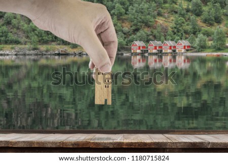 Hand choosing mini wood house model with blur red small houses with reflection and green trees background  A symbol for construction ,ecology, loan concepts
