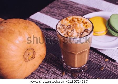 Latte with grated caramel in a glass with yellow and green macaroons on a white plate and a pumpkin on the table.