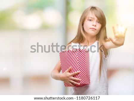 Young blonde toddler holding popcorn pack with open hand doing stop sign with serious and confident expression, defense gesture