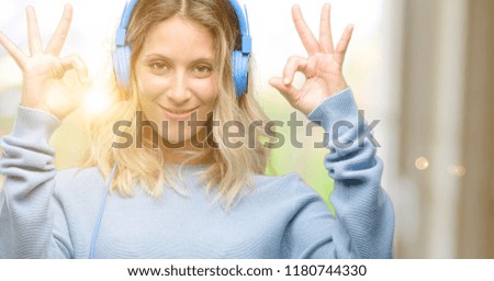 Young beautiful woman listening to music doing ok sign gesture with both hands expressing meditation and relaxation