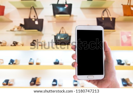Man use mobile phone, blur image of inside the bag and shoes store as background.