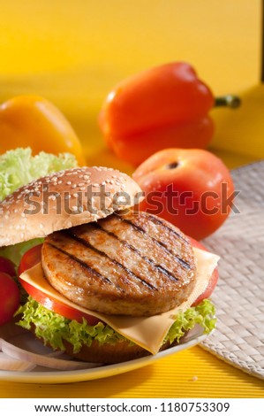 Chicken burger with bell pepper and lettuce with cherry red and yellow tomato on yellow background 