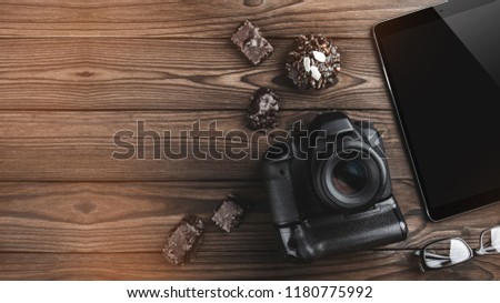 Camera photo, digital tablet, chocolate biscuits and eyeglasses on old wooden background. Top view, flat lay