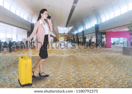 Picture of beautiful entrepreneur talking on a mobile phone while holding a suitcase in the airport hall