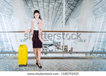 Picture of female entrepreneur using a smartphone while standing with a suitcase in the airport terminal