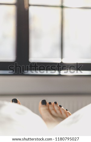 Female beautiful feet with a pedicure lie on the bed against the background of the morning window
