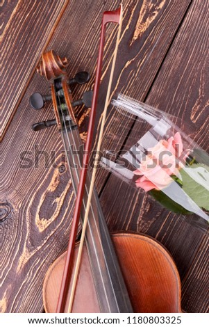 Violin and pink rose on wooden background. Vintage violin, fiddle stick and delicate flower on brown textured wood. Music and nature.