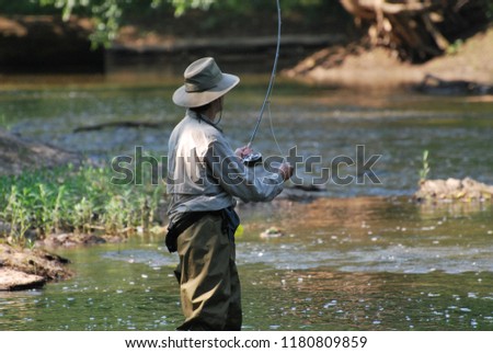 Man Fly Fishing in River, wearing fishing waders, hat, long sleeve shirt. 