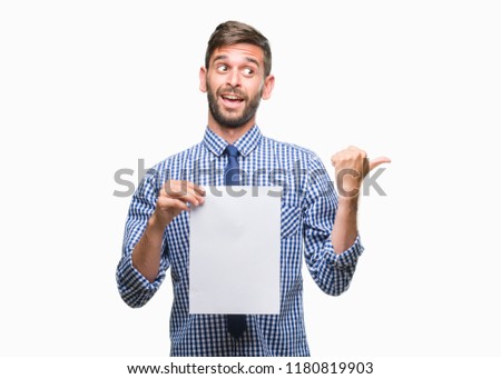 Young handsome man holding blank paper over isolated background pointing and showing with thumb up to the side with happy face smiling