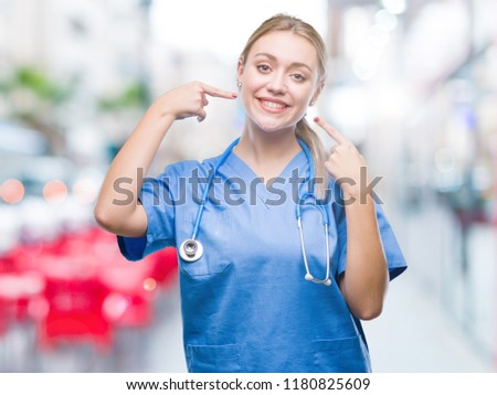 Young blonde surgeon doctor woman over isolated background smiling confident showing and pointing with fingers teeth and mouth. Health concept.