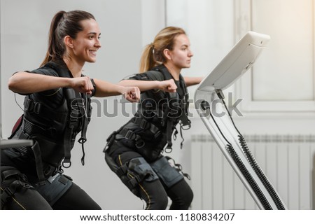 Young athletic women in EMS suits exercising in modern gym Royalty-Free Stock Photo #1180834207