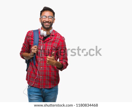Adult hispanic student man wearing headphones and backpack over isolated background doing happy thumbs up gesture with hand. Approving expression looking at the camera with showing success.