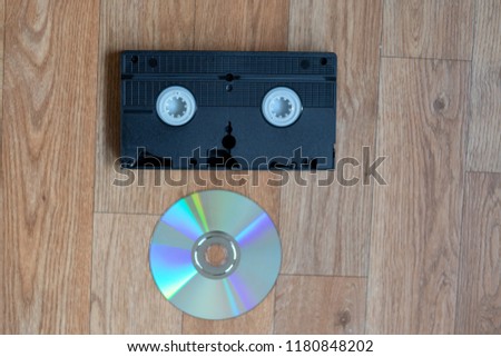 Old black videocassette beside a modern dvd on a wooden table 