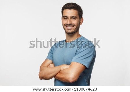 Portrait of attractive young sporty man in blue t-shirt standing with crossed arms isolated on gray background Royalty-Free Stock Photo #1180874620