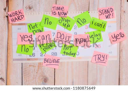 motivating phrases like Now, can do it, Yes, on colour sticky notes above demotivating text like I Can not, not Today,delay, give up posted to wall calendar on wooden board