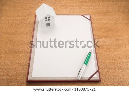 Blank paper, pen and house on a wooden table
