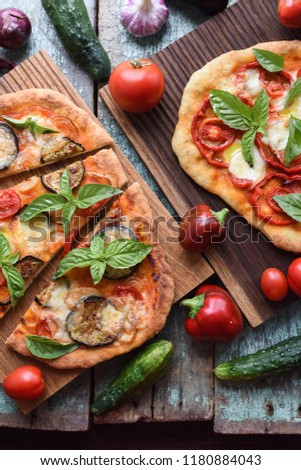 Vegetarian rustic pizzas. Freshly baked pizzas with aubergines, bell peppers and tomatoes on oak boards with raw vegetables above view