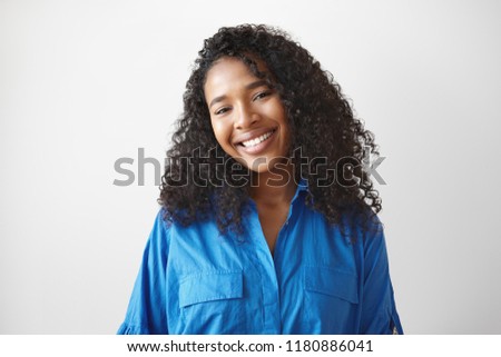 Joy, happiness, success, positiveness and good mood concept. Picture of fashionable beautiful young mixed race female with brown perfect skin, wavy black hairdo and broad smile posing in studio