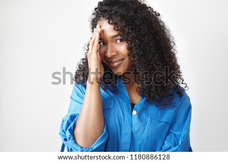 People, lifestyle, beauty and femininity concept. Isolated shot of gorgeous beautiful young dark skinned African woman with black curly hair and plush lips, smiling and covering face, feeling shy