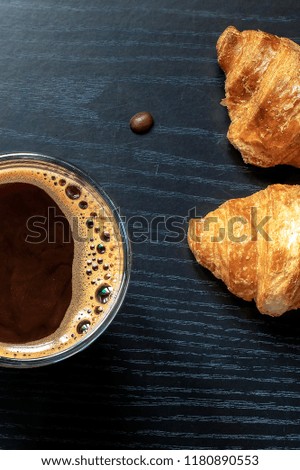 Croissants and coffee on a wooden board and a black wooden table. Free space for text.