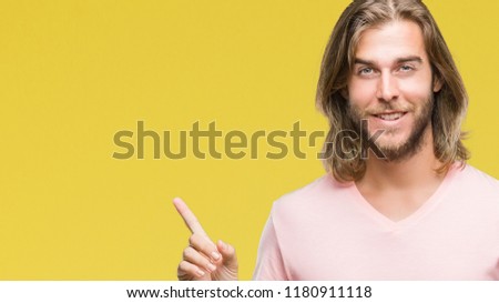 Young handsome man with long hair over isolated background with a big smile on face, pointing with hand and finger to the side looking at the camera.
