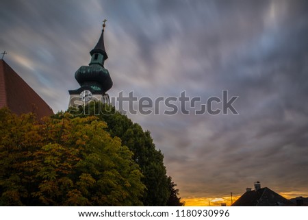 Long exposure picture of a bell tower in early morning, hiding behind the green and brown tree. Morning picture of a church in Seewalchen on Attersee, Austria.
