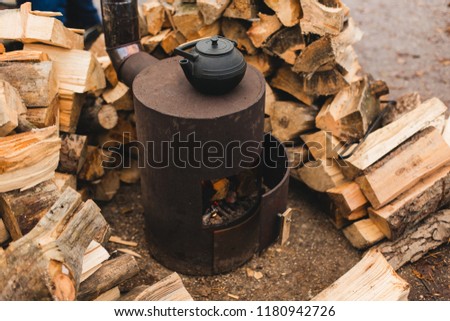 cast iron kettle for traditional oriental tea ceremony on burned stove with beautiful autumn oak leaves and stacked logs on the background